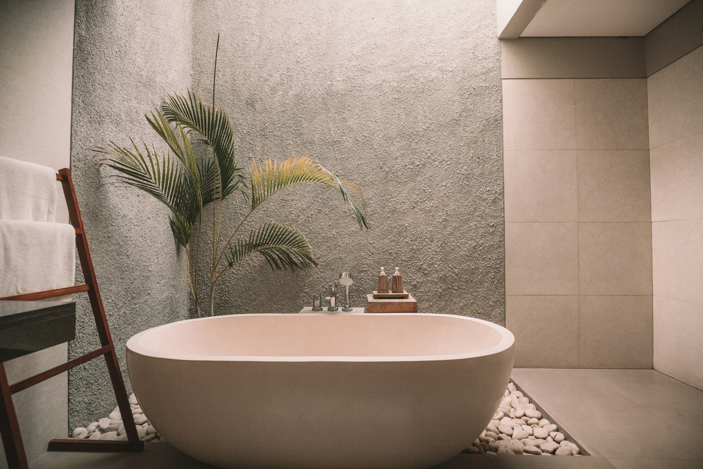 Freistehende Badewanne vor einer Natursteinwand mit Pflanzen