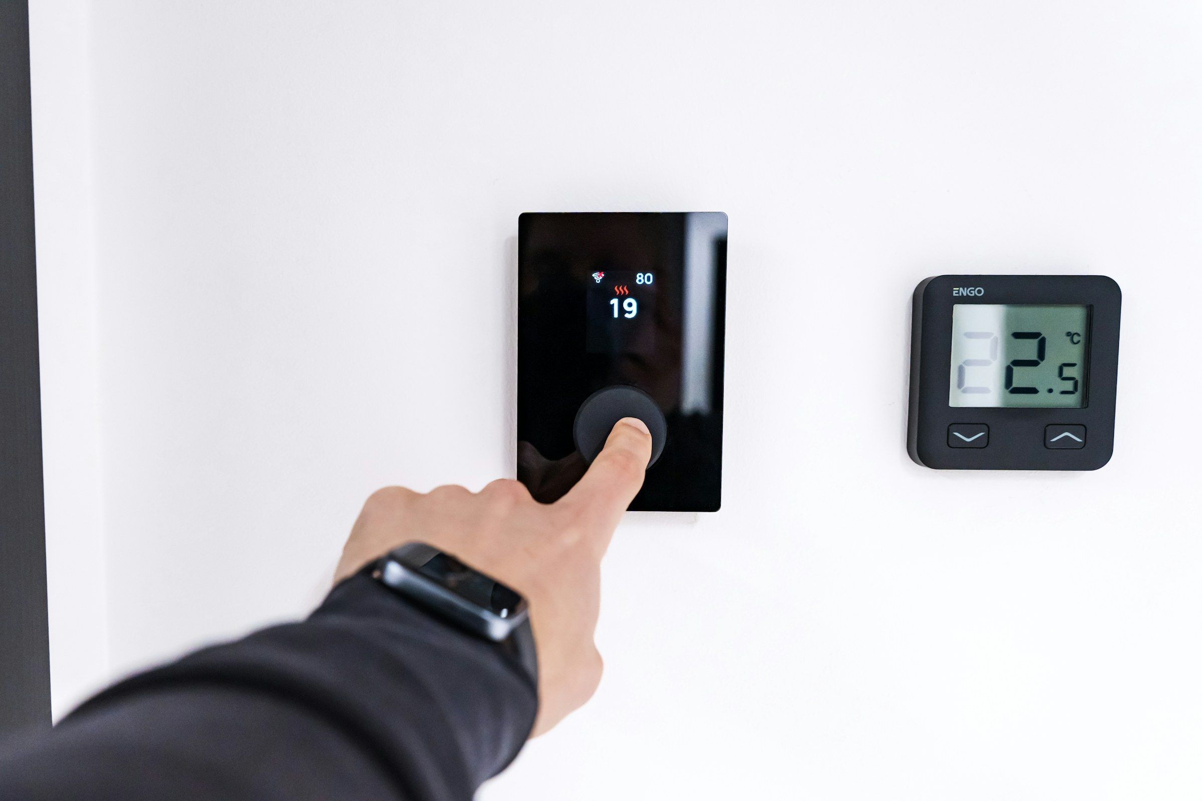 Hand stellt ein modernes digitales Raumthermostat an der Wand ein